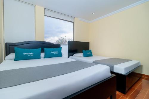 a bedroom with two beds with blue pillows and a window at Hotel Ayenda Normandy in Bogotá