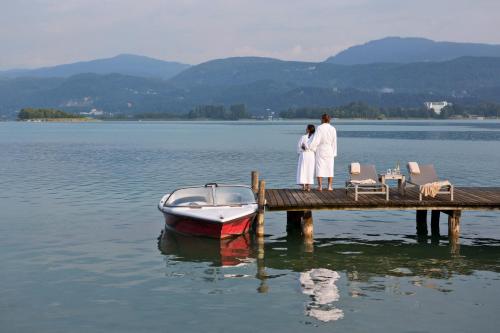 two people standing on a dock next to a boat at Hotel Linde in Maria Wörth