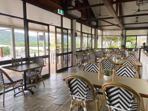 un restaurante con mesas, sillas y ventanas en Colonial Palms Motor Inn, en Airlie Beach