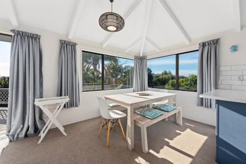 uma sala de jantar com mesa, cadeiras e janelas em The Blue Beach House em Mount Maunganui