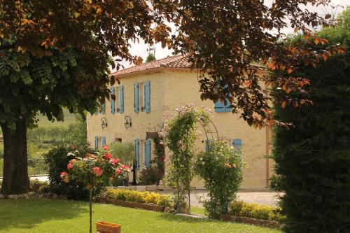 un bâtiment avec des fenêtres bleues et des fleurs dans une cour dans l'établissement Maison d'Hôtes Las Baillargues de Haut, à Mouchan