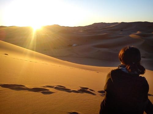 a woman standing in the desert watching the sunset at Riad Dar Ouzine in Merzouga