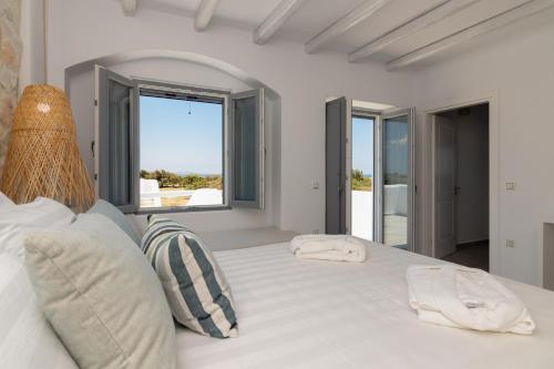 a white bedroom with a large white bed with windows at Isalos Villas Naxos in Naxos Chora