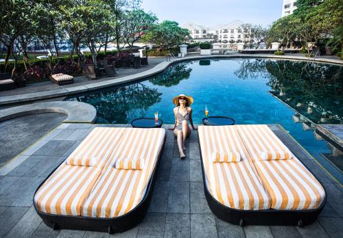 Una mujer con sombrero está de pie entre dos bancos en una piscina en InterContinental Hanoi Westlake, an IHG Hotel en Hanoi