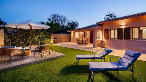 a yard with chairs and an umbrella and a house at Villa Gea 8, Emma Villas in Costa Rei