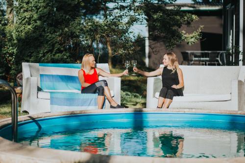 two women sitting next to a pool with glasses of wine at Kroņkalniņi in Lapmežciems