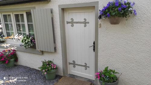 białe drzwi z kwiatami na boku domu w obiekcie Le Memagne w mieście Florenville