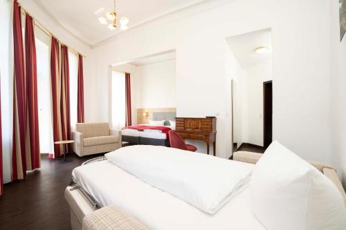 a white bedroom with a bed and a chair at Hotel National in Bamberg