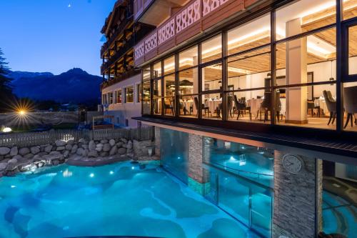 a hotel with a swimming pool in front of a building at Croce Bianca Leisure & Spa Hotel in Canazei