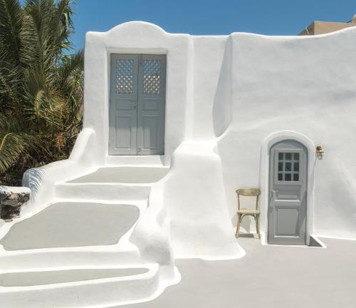 a white house with a blue door and stairs at AQUA SERENITY LUXURY SUITES SANTORINI in Foinikiá