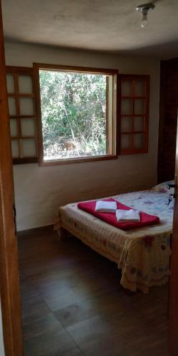 a bedroom with a bed with red pillows and a window at Chalé 1 - Recanto Shambala in São Thomé das Letras