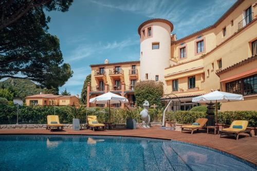 una piscina frente a un edificio con sillas y sombrillas en Ermitage de l'Oasis & Spa - Cannes Mandelieu, en Mandelieu-la-Napoule