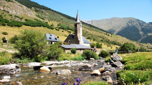 een kerk op een heuvel naast een rivier met rotsen bij Pension casat in Salardú