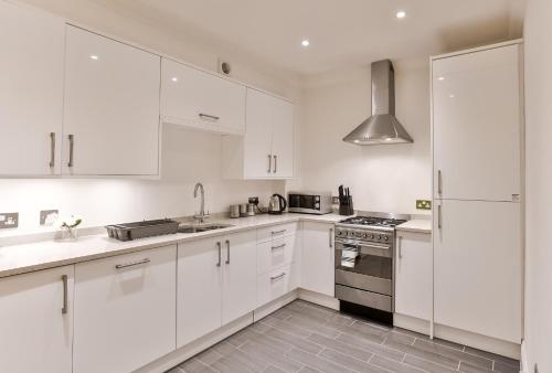 a white kitchen with white cabinets and a stove at KVM - Jubilee Mansions Apartment by KVM Stays in Peterborough