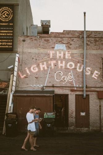 two people walking in front of a building with a sign at ITH Hermosa Beach Surf Hostel LAX in Hermosa Beach