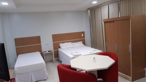 a room with two beds and two red chairs at Hotel Coimbra in Tucuruí