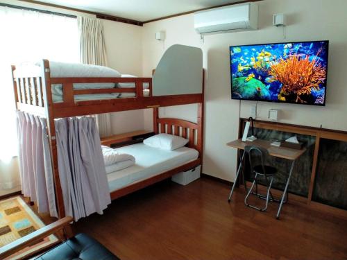 1 Schlafzimmer mit Etagenbetten, einem Schreibtisch und einem TV in der Unterkunft Hiroshima Saijo Youth Hostel in Higashihiroshima