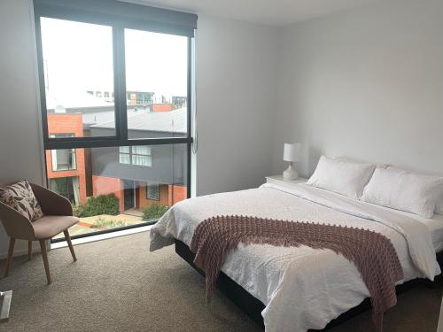 a bedroom with a bed and a chair and a window at One central apartments city centre in Christchurch