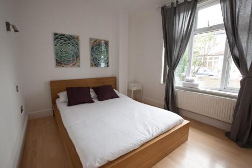 una camera da letto con un letto con lenzuola bianche e una finestra di Tooting Rooms by DC London Rooms a Londra