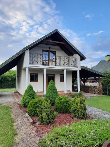 a white house with a balcony and some bushes at Domek Chmiel I nad Jeziorem Tarnobrzeskim in Chmielów