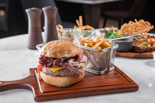 a sandwich on a wooden plate with a basket of fries at Park Inn by Radisson, Riyadh in Riyadh