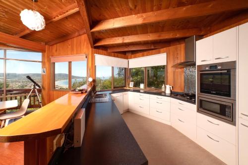 a kitchen with white cabinets and wood ceilings and windows at Kinoie Mornington - OCEANVIEW in Mount Martha