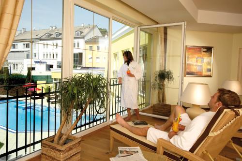 a woman standing on a balcony with a man sitting on a couch at Parkhotel in Bad Schallerbach
