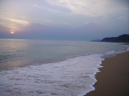 a beach with the sun setting over the ocean at Hotel Loukas Vrachos in Paralia Vrachou