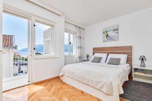 a white bedroom with a bed and large windows at Waikiki Beach House in Tivat