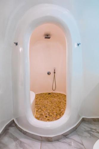 a bathroom with a large white bath tub with a round mirror at Santorini Delux in Imerovigli
