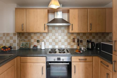 a kitchen with wooden cabinets and a stove top oven at KVM - Peacock Apartment close to town by KVM Stays in Peterborough