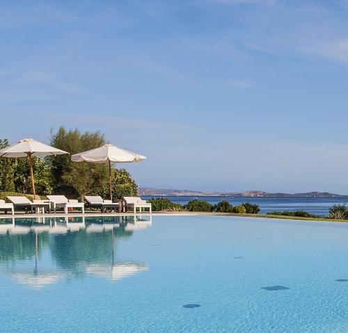basen z parasolami i krzesłami oraz wodą w obiekcie L'Ea Bianca Luxury Resort w mieście Baja Sardinia
