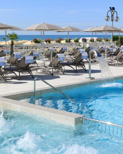 a swimming pool with chairs and a water fountain at Hotel Cavalieri Palace & Suites in Lido di Jesolo