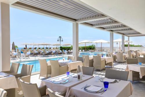 un restaurante con mesas y sillas blancas y una piscina en Hotel Cavalieri Palace, en Lido di Jesolo