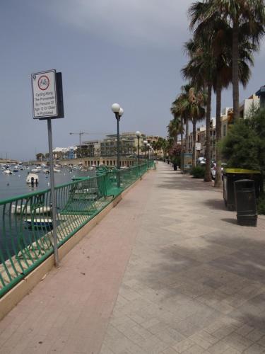a sidewalk next to the water with palm trees at Modern Two Bedroom Sea View Apartment in Marsaskala