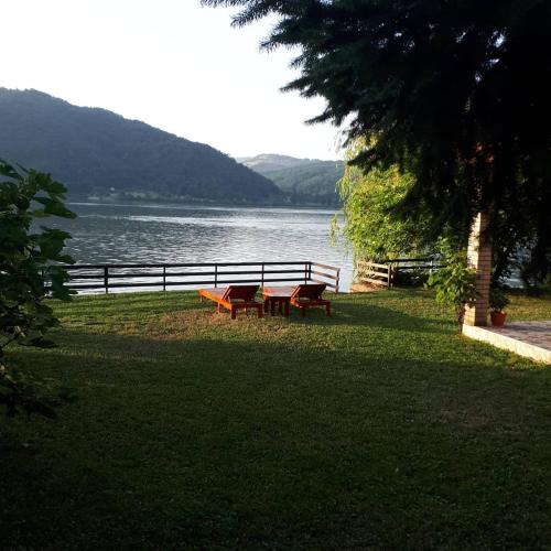 two picnic tables in the grass near a body of water at Dedin raj in Golubac