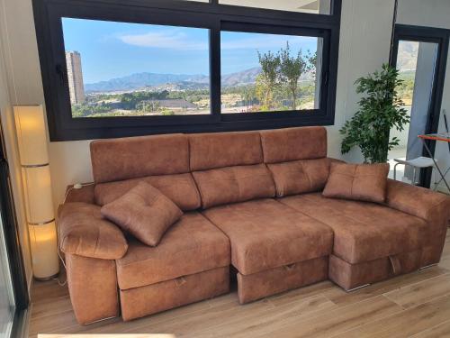 a brown couch in a living room with a large window at Sunset Waves Benidorm by KalmaRent in Benidorm