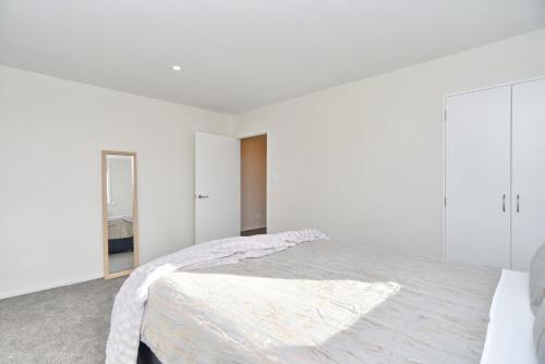 a white bedroom with a bed and a mirror at Lavandula 4 - Christchurch Holiday Homes in Christchurch