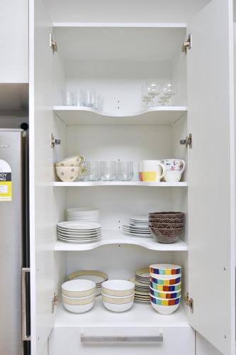 a white cabinet filled with plates and bowls at Lavandula 4 - Christchurch Holiday Homes in Christchurch