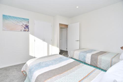 two beds in a room with white walls at Lavandula 4 - Christchurch Holiday Homes in Christchurch