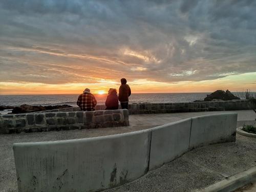 three people sitting on a wall watching the sunset at El Rincon de Las Pleyades in El Quisco