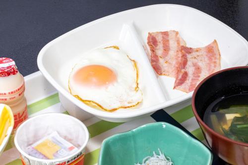 a table with a plate of food with an egg and bacon at Tabist Hotel Takagiya Iwaki in Hisanohama