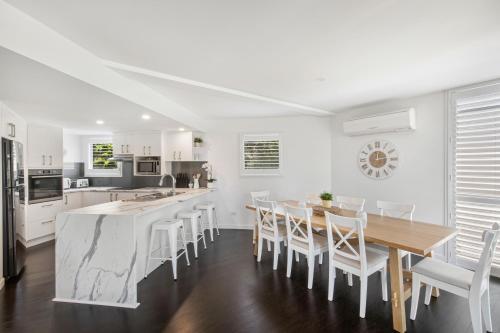 a white kitchen with a wooden table and chairs at Castaway Cove Beachfront Home by Stay Noosa in Marcus Beach