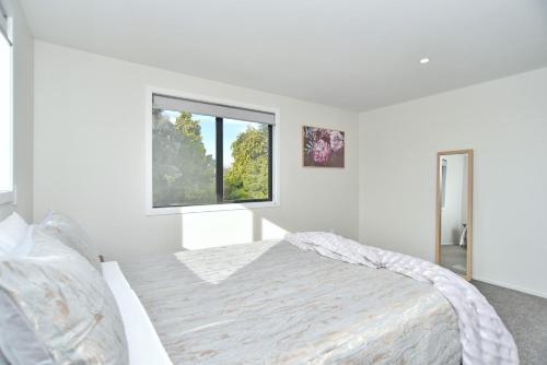a white bedroom with a bed and a window at Lavandula 3 - Christchurch Holiday Homes in Christchurch