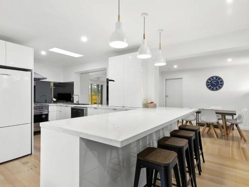 a white kitchen with a large white counter and stools at Puebla Casa 17 in Torquay