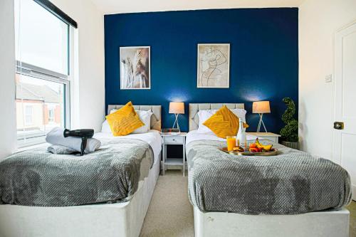 a bedroom with two beds and a blue wall at Cosy House with Free Parking, Smart TVs & Garden by Yoko Property in Northampton