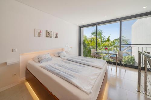 a white bedroom with a bed and a balcony at Quinta Golfinho in Arco da Calheta