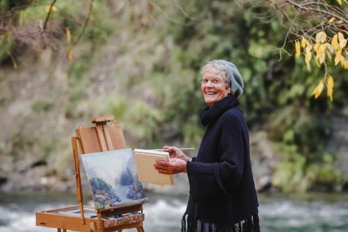 an older woman is standing next to an art easel at River Valley Lodge in Taihape