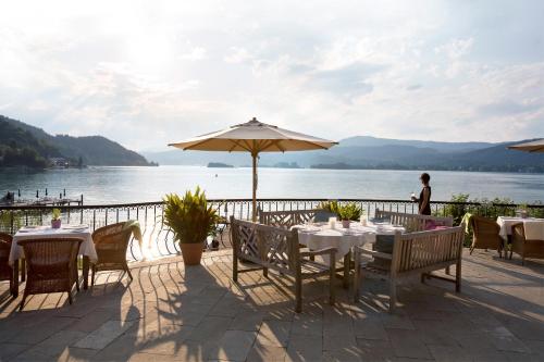 a woman standing on a patio with tables and an umbrella at Hotel Linde in Maria Wörth