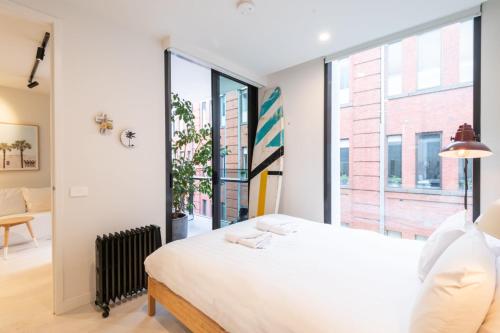 a bedroom with a white bed and a large window at Trendy 1 Bedroom Apartment in the Heart of Collingwood in Melbourne